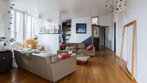 A spacious living room with a sofa, coffee table, and a bookshelf. - Le Rooftop Aux Puces - Terrasse rooftop (Saint Ouen)