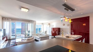 Ett modernt vardagsrum med ett stort fönster, en vit soffa, en matplats med ett bord för två personer och en röd accentvägg.