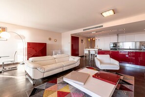 Ein modernes Wohnzimmer mit einem weißen Sofa, einem Couchtisch und einem roten Akzent. Es gibt eine Küchenzeile mit roten Schränken und einem Esstisch.