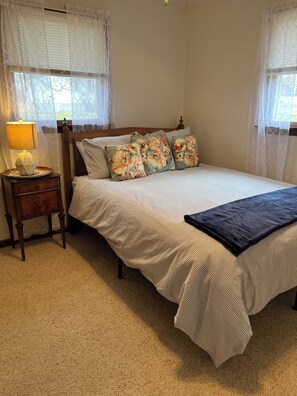A bedroom with a bed, a nightstand, a lamp, and a window with curtains.