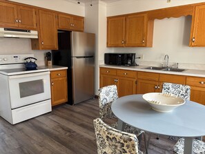 A kitchen with wooden cabinets, a stainless steel refrigerator, a microwave, and a sink. There is a table with a bowl on it and two patterned chairs. - Brand new listing 1 mile from the quaint villages of Marblehead & Lakeside (Lakeside)