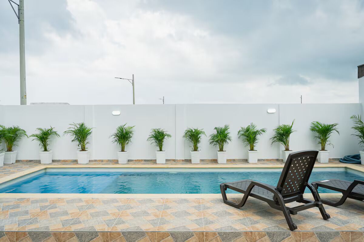 Una piscina con sillones de descanso, plantas en macetas y una pared blanca con líneas eléctricas.