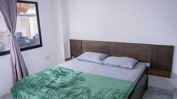 Un dormitorio con una cama, una manta verde, un cabecero de madera y una ventana con cortinas.