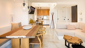 Een moderne woonkamer met een houten eettafel, een witte bank en een aan de muur bevestigde televisie.