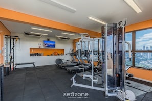 Un gimnasio con equipamiento de ejercicio, una banca y un televisor en la pared.