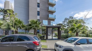 Een modern gebouw met een glazen ingang, omgeven door palmbomen en geparkeerde auto's.