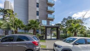 Un edificio moderno con entrada de vidrio, rodeado de palmeras y automóviles estacionados.