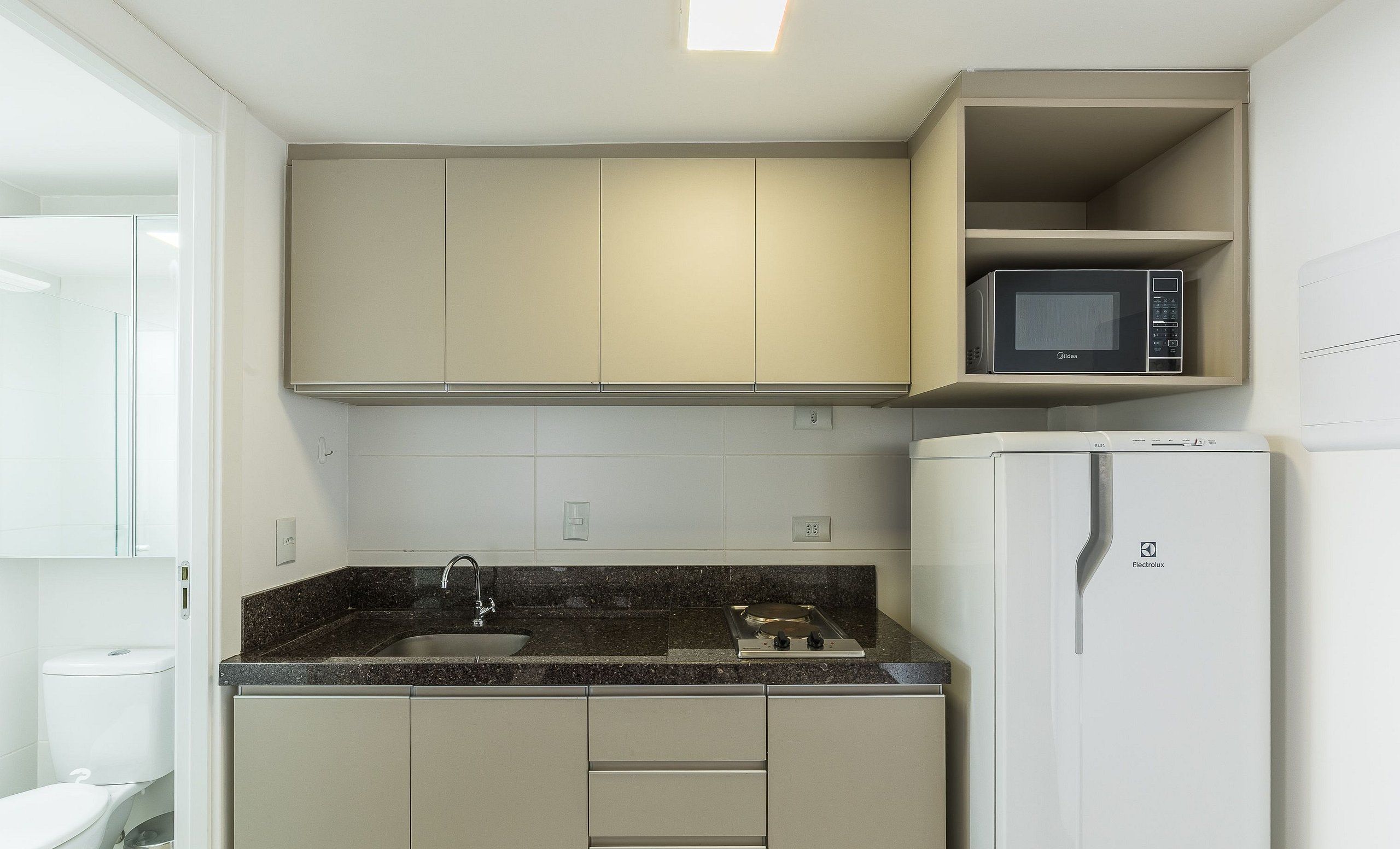Eine kompakte Küche mit integriertem Mikrowellenherd, einem Kühlschrank und einem Spülbecken mit Granit-Arbeitsplatte.