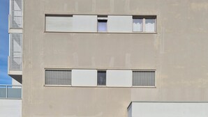 Ein modernes Gebäude mit flachem Dach, großen Fenstern und einer gepflasterten Eingangszone mit Rasen im Vordergrund.