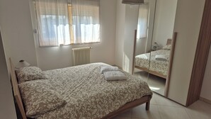 Ein Schlafzimmer mit Bett, Nachttisch, Lampe, Heizkörper und Spiegel.