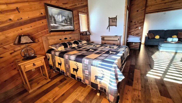 Une chambre confortable dans un chalet en rondins, avec un grand lit, une table de chevet, une commode et un tableau accroché au mur.
