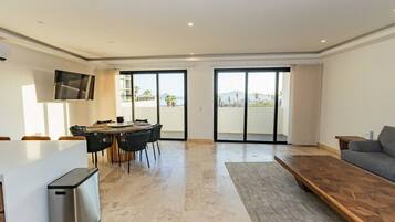 A modern living room with a dining area, a sofa, a TV, and a balcony with a view.