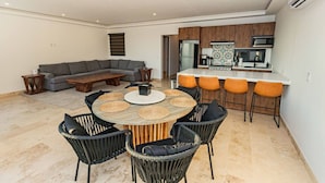 Una sala de estar moderna con un sofá seccional gris, una mesa de centro de madera y una mesa de comedor redonda con posavasos tejidos y sillas negras.