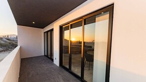 Un balcón con vista al atardecer, una puerta de vidrio y una mesa con sillas.