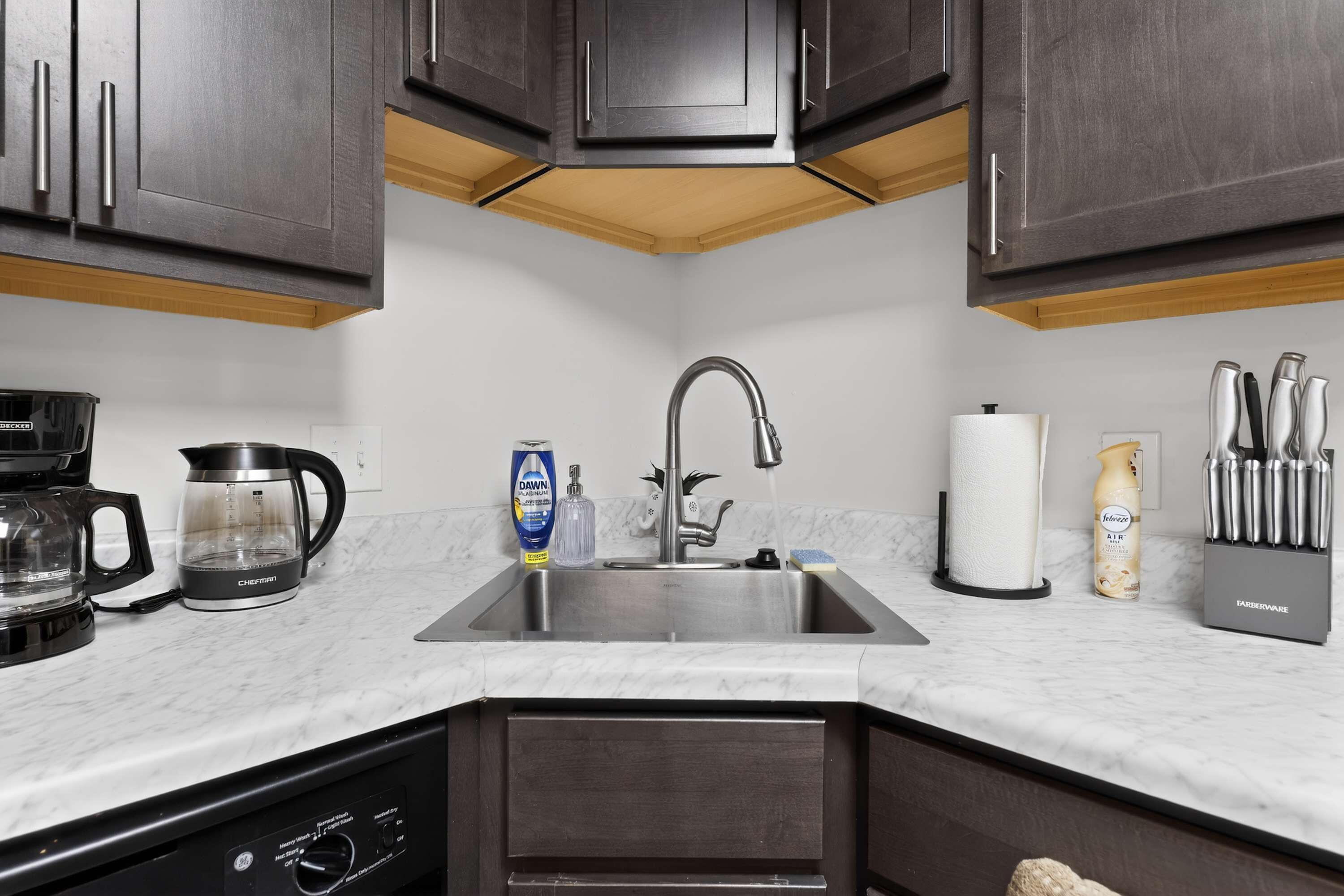 A modern kitchen with dark cabinets, a stainless steel sink, a coffee maker, and a dish soap bottle.