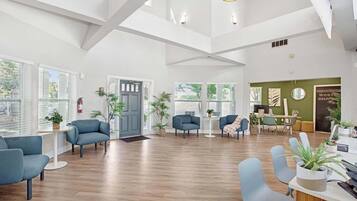 A spacious room with a wooden floor, a grey door, and a seating area with blue chairs.