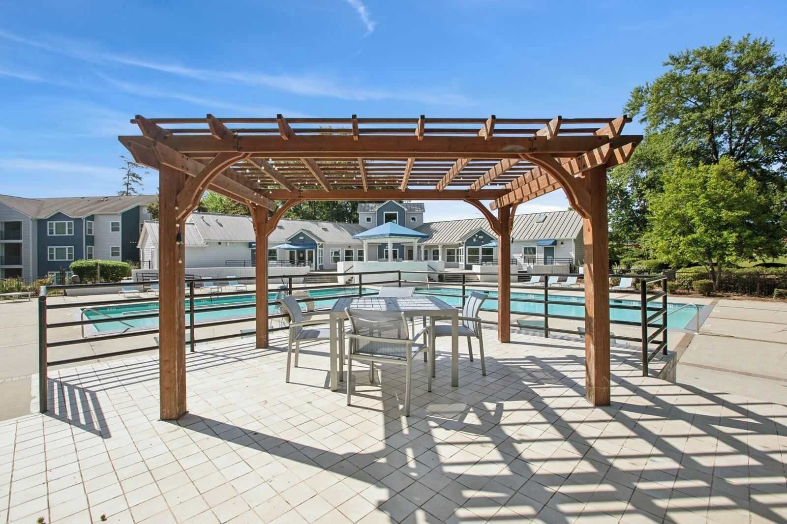A covered outdoor area with a pool, seating, and a view of residential buildings in the background.