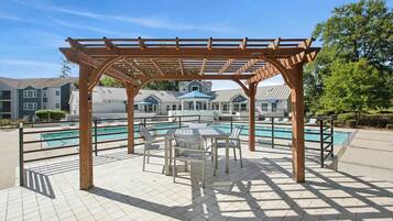 A covered outdoor area with a pool, seating, and a view of residential buildings in the background.