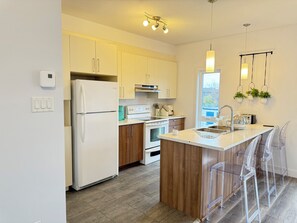 A modern kitchen with white cabinets, a built-in oven, a refrigerator, and a wooden island with bar stools. - Premium comfort, stylish, spacious, and fully equipped apartment (Gatineau)