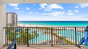 Ein Balkon mit Blick auf einen Strand, einen Poolbereich und ein hohes Gebäude.