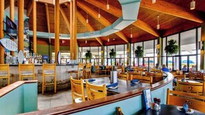 Ein geräumiges Restaurant mit hohen Decken, Holzbalken und großen Fenstern.