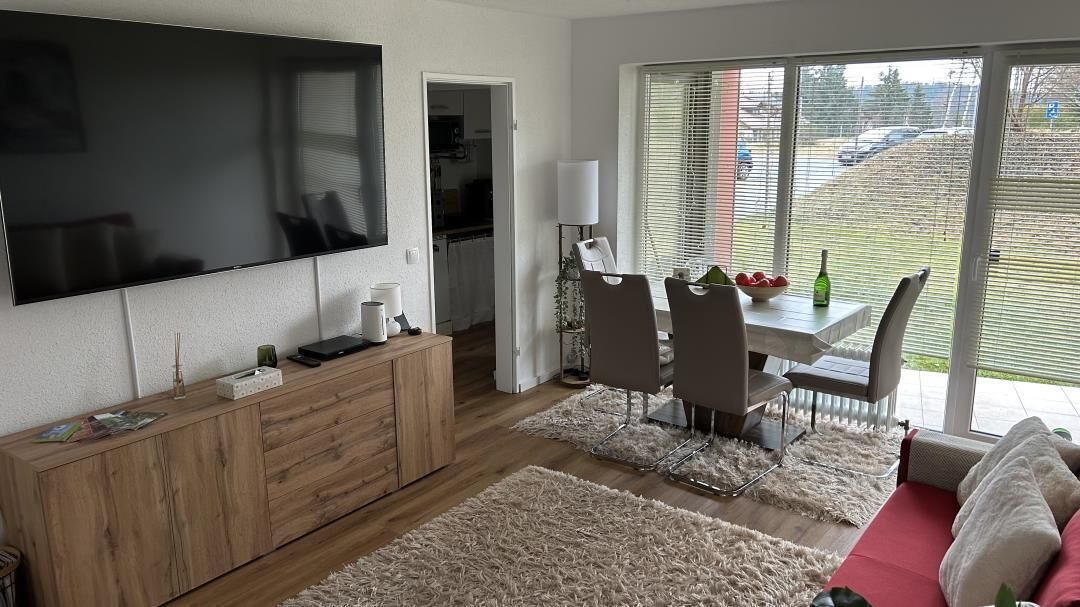 Un salon moderne avec un téléviseur à écran plat, un meuble en bois, une table à manger avec des chaises et un canapé rouge.