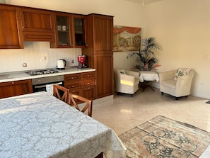 A kitchen with wooden cabinets, a gas stove, and a coffee maker. There is a dining table with chairs and a rug. - BERTO'S HOUSE2 (TREPORTI)