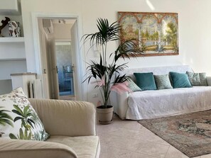 A living room with a beige sofa, a white sofa with teal cushions, a large potted plant, and a painting on the wall. - BERTO'S HOUSE2 (TREPORTI)