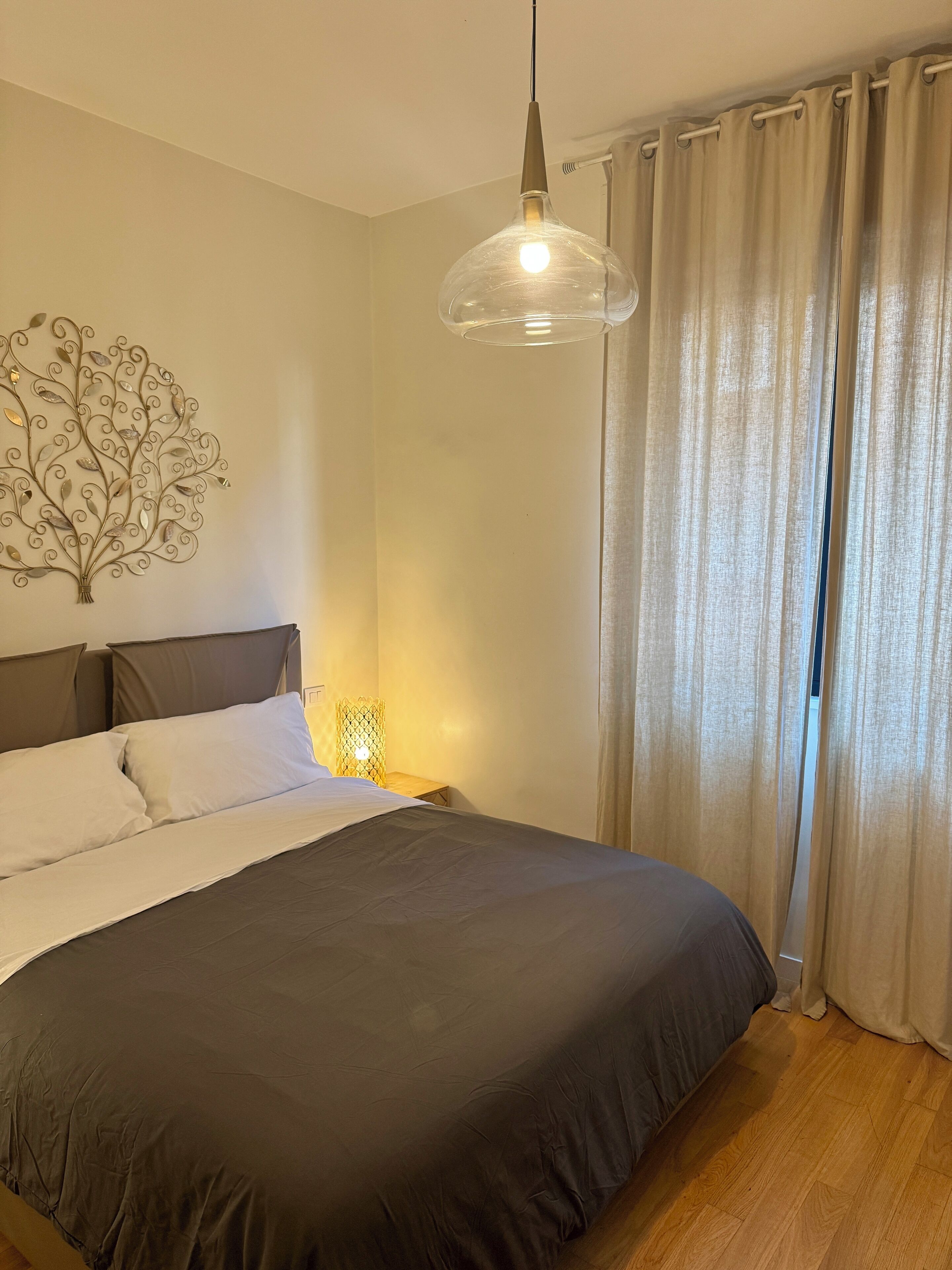 A bedroom with a bed, a wall-mounted light fixture, and a curtain.