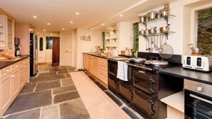 A modern kitchen with a stone floor, stainless steel appliances, and a glass shelf with cookware. - Ladye Park (Liskeard)