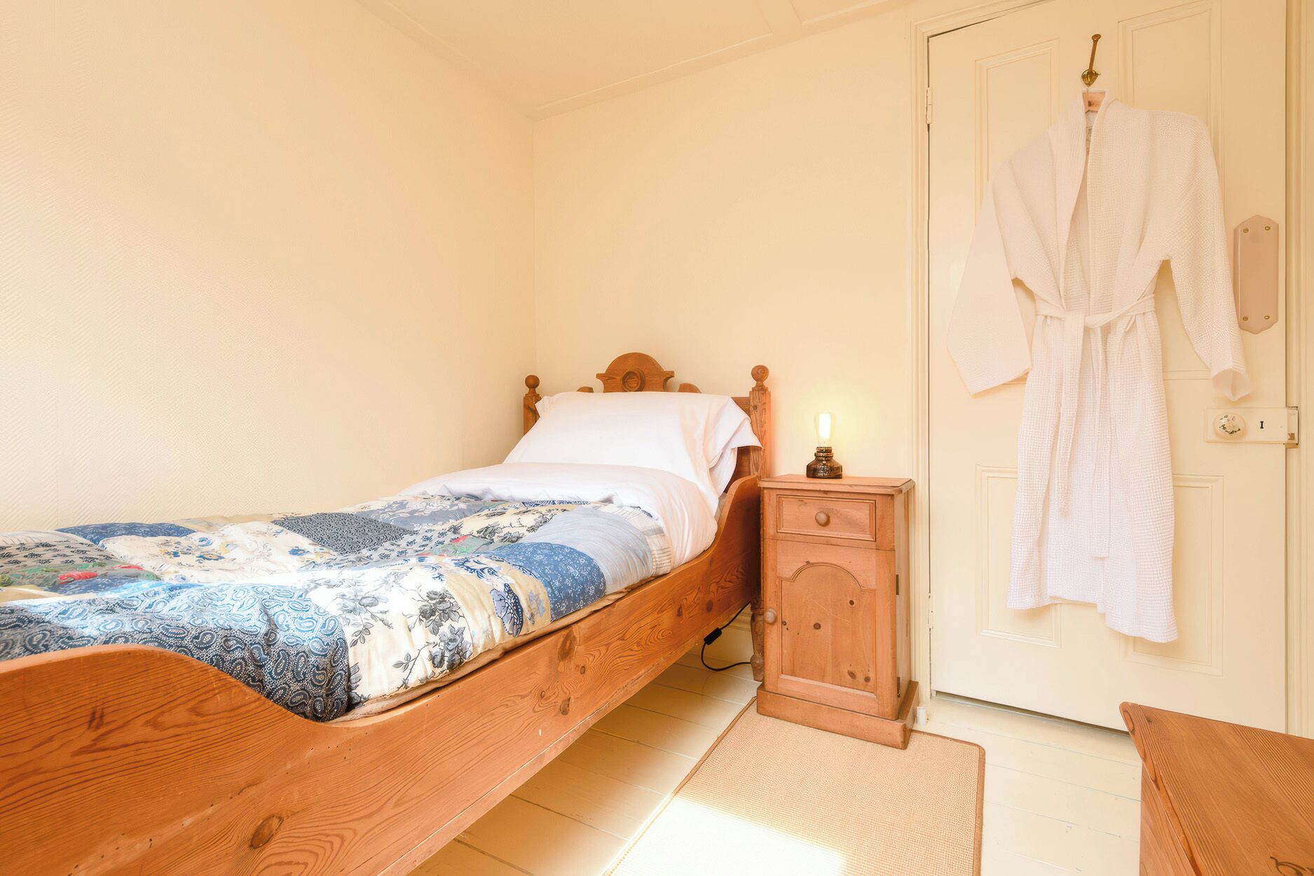A bedroom with a wooden bed, a bedside table, a nightstand, and a robe hanging on a door.