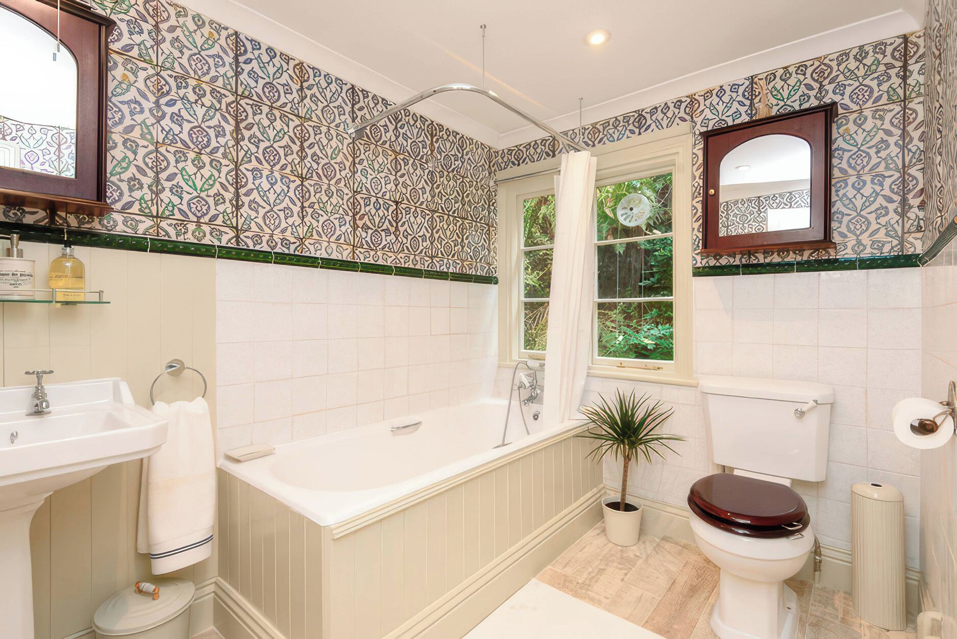 A bathroom with a bathtub, toilet, sink, and a window with a view of greenery.