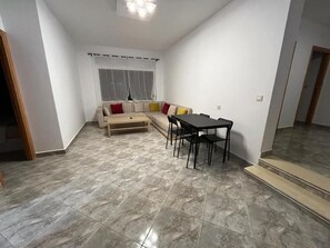 A living room with a sofa, a dining table with chairs, and a window with curtains. - capuchino sanya (Tanger)