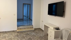 Une pièce dotée d’un téléviseur à écran plat fixé au mur, d’un bureau blanc avec des tiroirs et d’une chaise blanche.