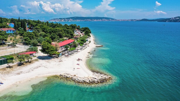 Une zone côtière avec une plage, une mer d’un bleu limpide et des bâtiments aux toits rouges.