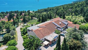 Un hôtel situé sur la côte, avec un toit recouvert de tuiles rouges, entouré d’une végétation luxuriante et offrant une vue sur la mer.