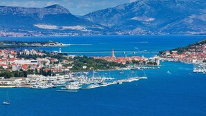 Une ville côtière dotée d’un port de plaisance, avec des montagnes en arrière-plan et un ciel dégagé.