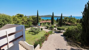 A courtyard with a paved pathway leading to a building with a red roof, surrounded by greenery and cypress trees. - Medena Apartments Superior two-room apartment Seaside A2+2 for 4 persons (Seget Donji)