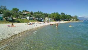 Een kiezelstrand met helder water, parasols en mensen.