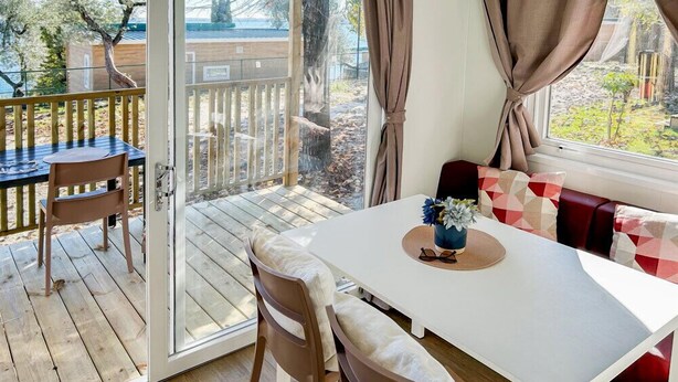 Et værelse med en skydedør, der fører ud til en terrasse, et hvidt bord med stole, og en sofa med rødt og hvidt mønster.