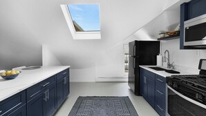 Eine moderne Küche mit dunkelblauen Schränken, einer weißen Arbeitsplatte, einem Oberlicht, einem schwarzen Kühlschrank und einem Gasherd.