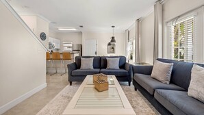 A living room with a sofa, a coffee table, and a kitchen in the background. - 4BR Townhome Near Disney at Lucaya Village (Kissimmee)