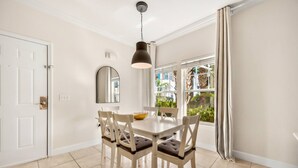 A dining area with a white table, four chairs, a hanging light fixture, a mirror, and a window with curtains. - 4BR Townhome Near Disney at Lucaya Village (Kissimmee)