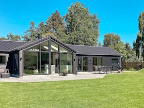 Ett modernt hus med ett stort glashus, en uteplats med utemöbler och en välskött gräsmatta.