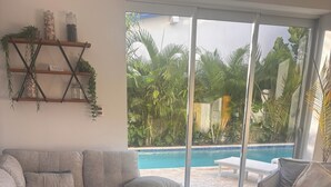 Un soggiorno moderno con un divano angolare grigio, un tavolino in legno e una porta in vetro che si apre su una zona piscina.