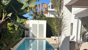Una piscina circondata da un prato curato, con un edificio bianco e una palma sullo sfondo.