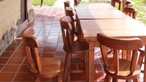 An outdoor dining area with wooden tables and chairs, a thatched roof, and a view of the surrounding landscape. - POSADA EL ARTESANO DE RAQUIRA (Ráquira)