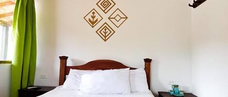 A neatly made bed with a wooden headboard, a green throw blanket, and a wall with geometric patterns.