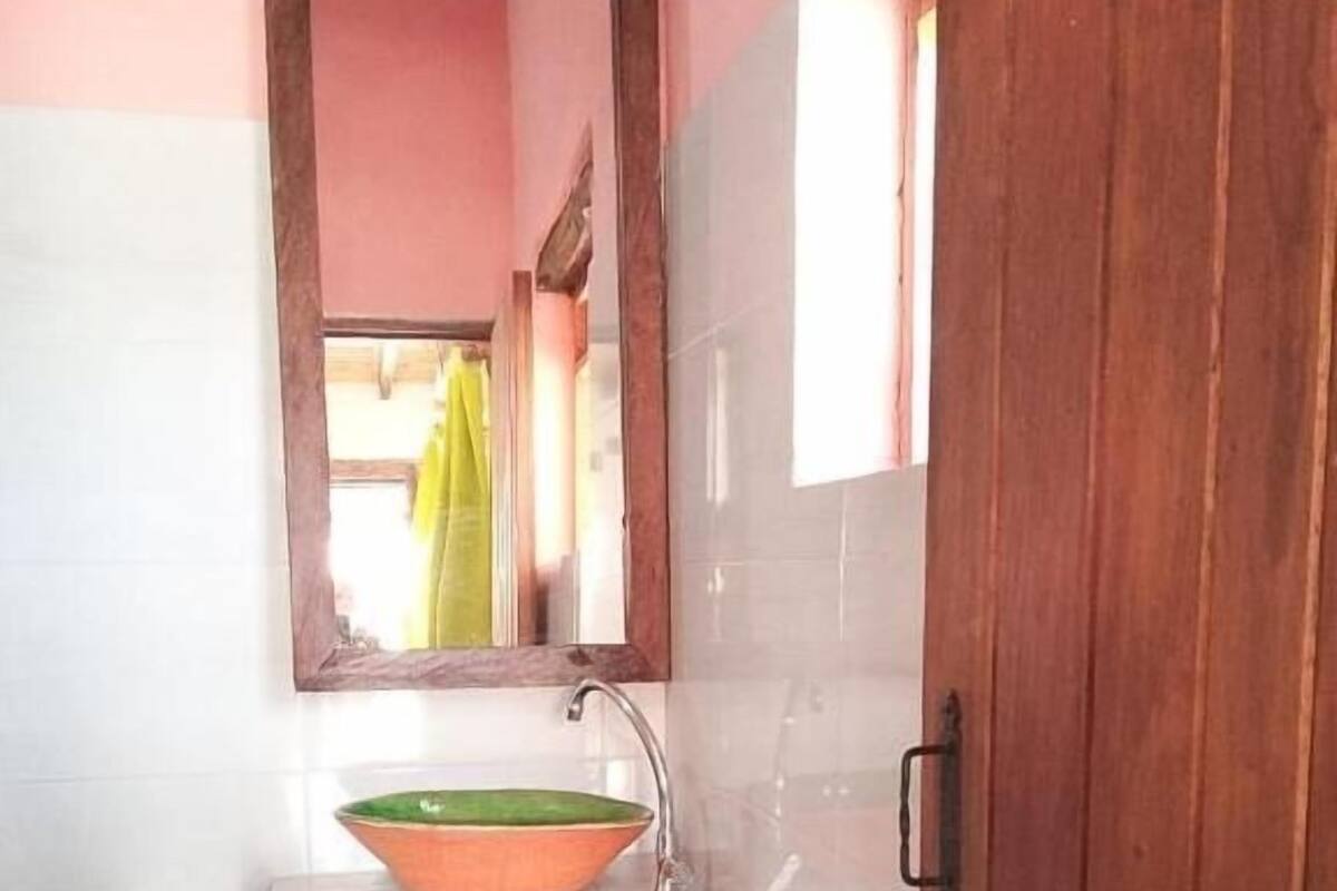 Un baño con un lavabo blanco, un recipiente verde y naranja, un espejo y una puerta de madera.