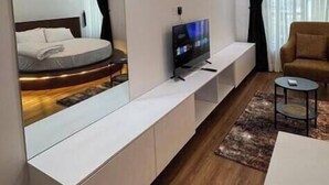 A modern hotel room with a large mirror, a flat-screen TV, a sofa, and a small round table. - 3 Bedroom En-Suite, Wi-Fi, Secured, 24/7 Power (Lagos)